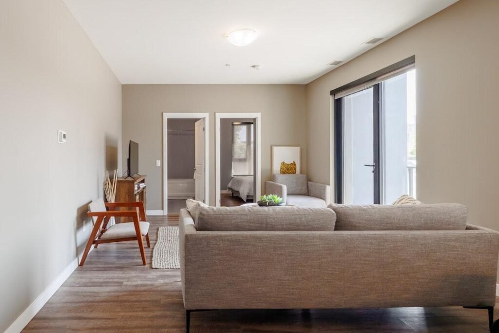Sala de estar com piso amadeirado, sofá e poltrona junto à porta de vidro.